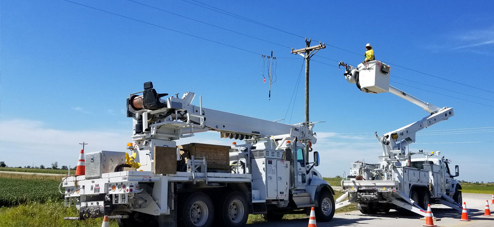 Two service trucks working on power line in a rural setting
