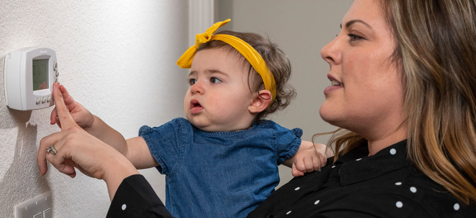 mom-holding-daughter-adjusting-the-thermostat-on-wall