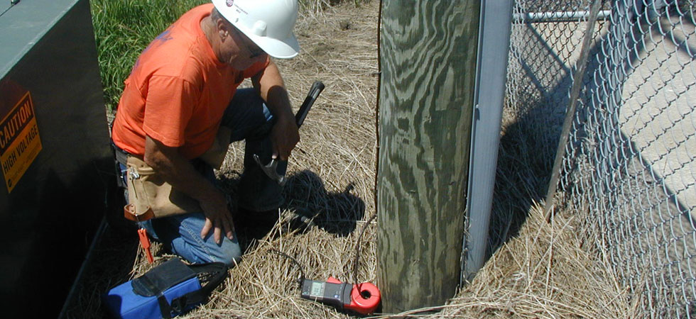 Worker testing current with meter at the base of a power pole