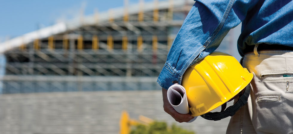 Close-up of man holding yellow hard-hat and blueprints on a job site