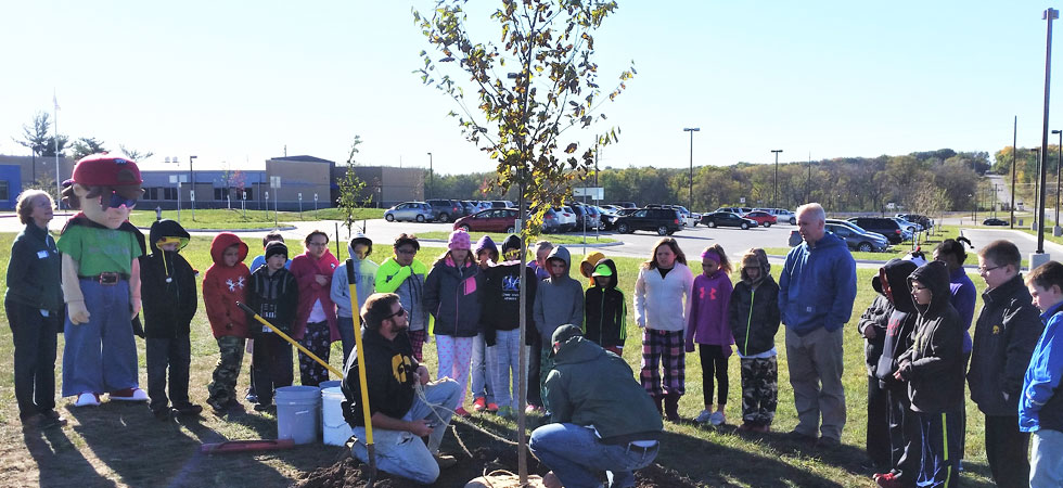 Group of kids watch two men plant a tree outdoors